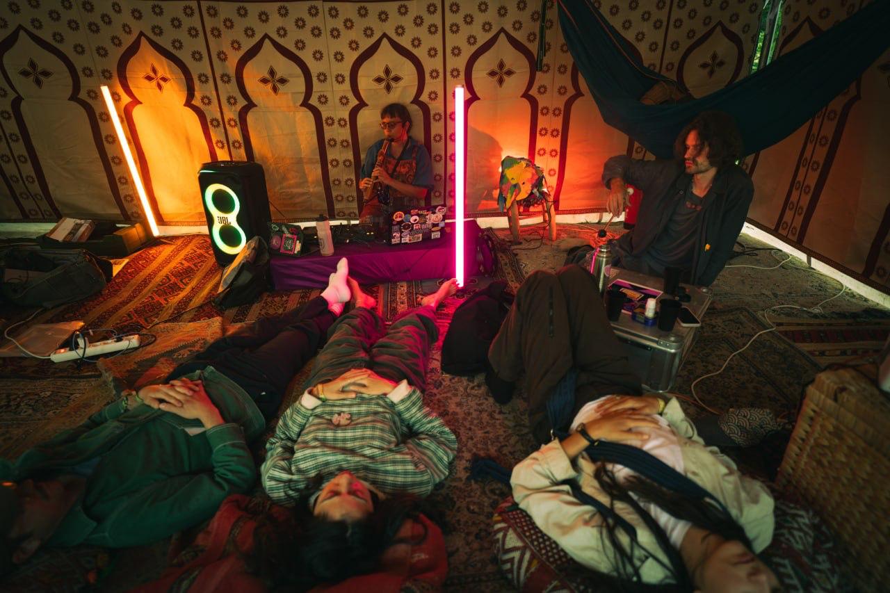 Artizens resting and making music together inside a decorated tent